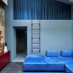 Časť obývacej izby s modrou sedačkou a rebríkom vedúcim do spálne.