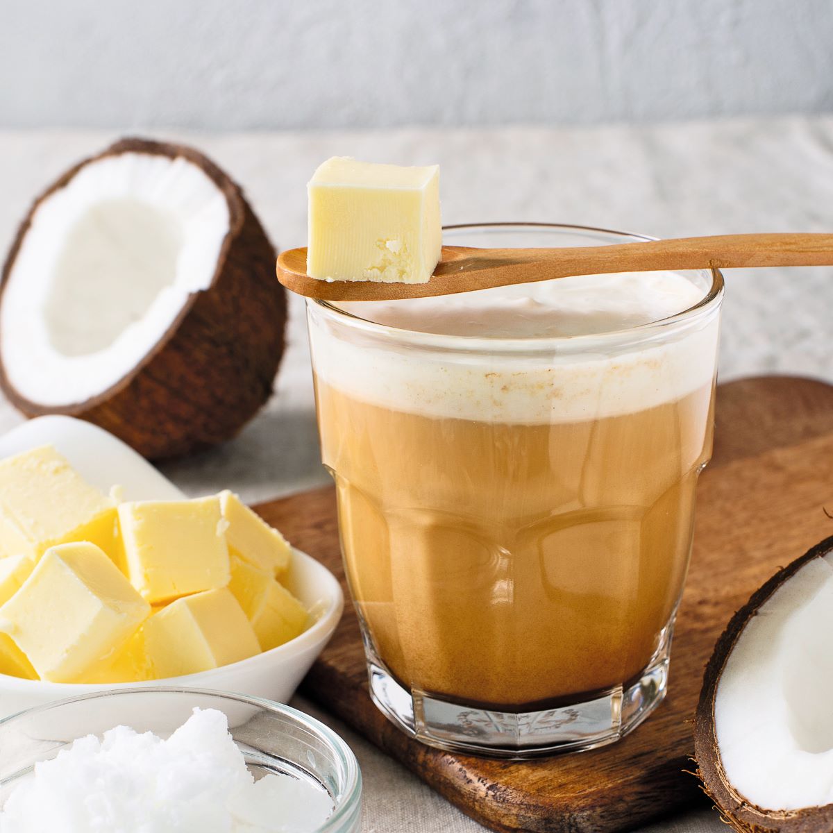 Pohár s ochutenou kávou pri kockách masla a kokose.