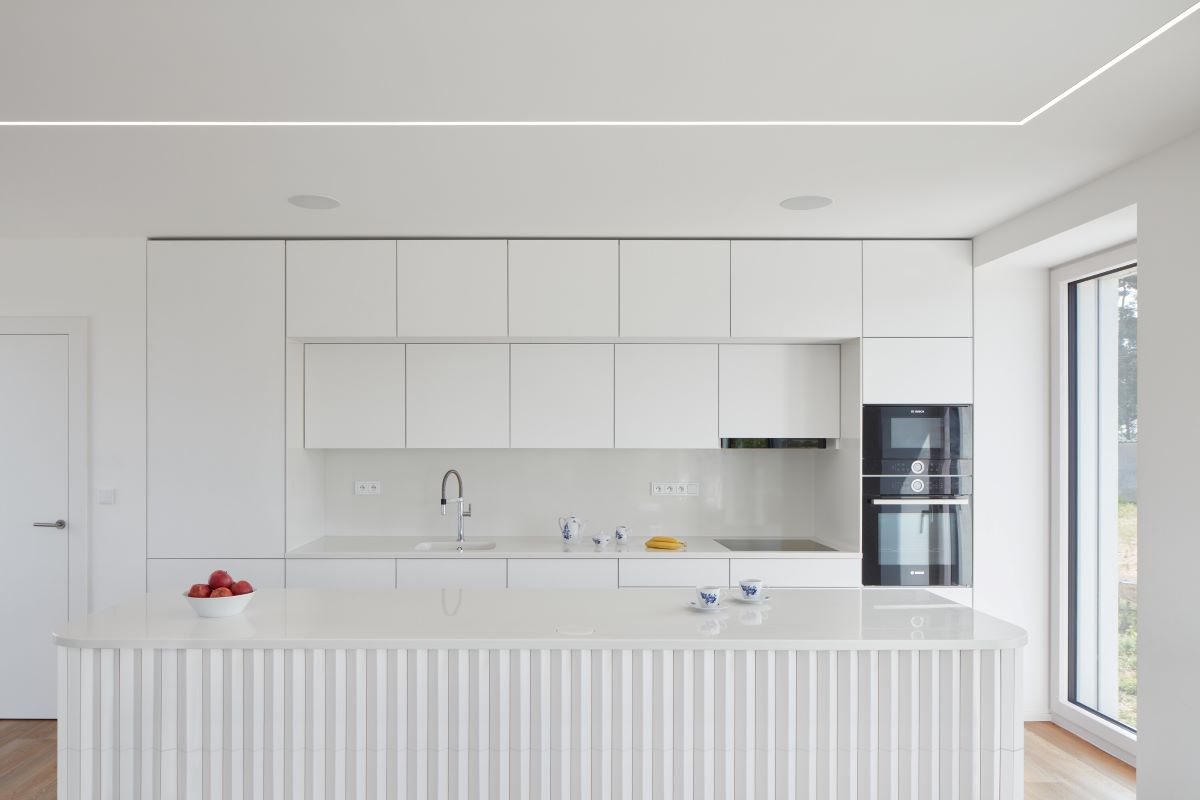 Záber na bielu minimalistickú kuchyňu s ostrovom.