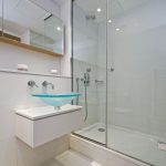 Časť kúpeľne so sprchovacím kútom a skleneným umývadlom na skrinke.