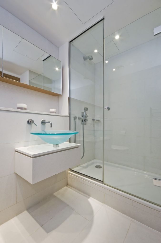 Časť kúpeľne so sprchovacím kútom a skleneným umývadlom na skrinke.
