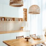 Bielo-drevená kuchyňa s linkou, stolom a ratanovými svietidlami.