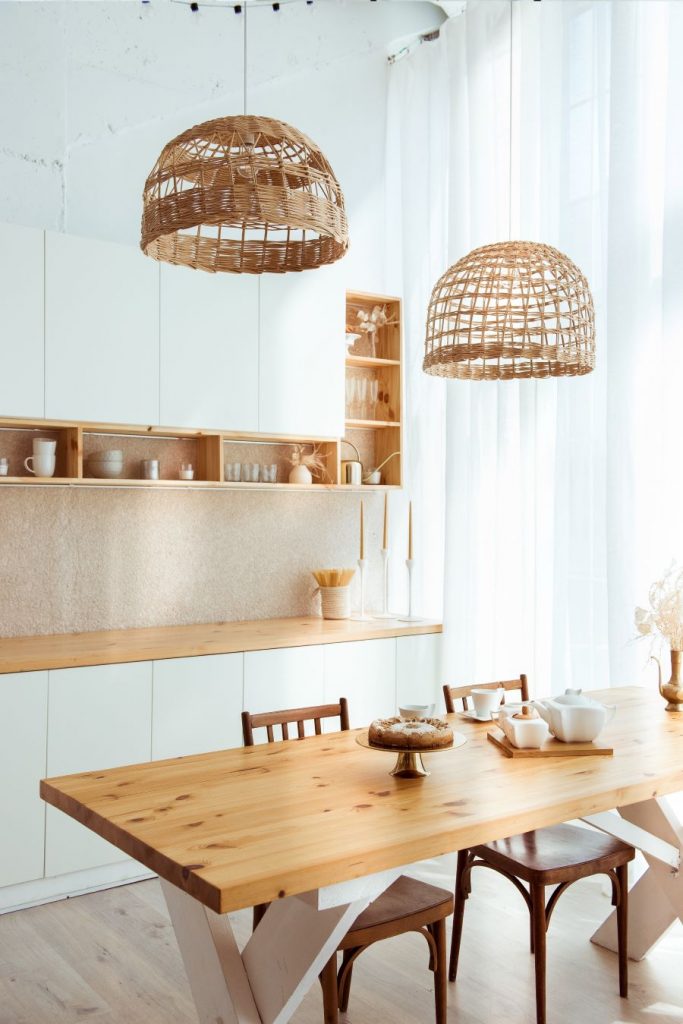 Bielo-drevená kuchyňa s linkou, stolom a ratanovými svietidlami.