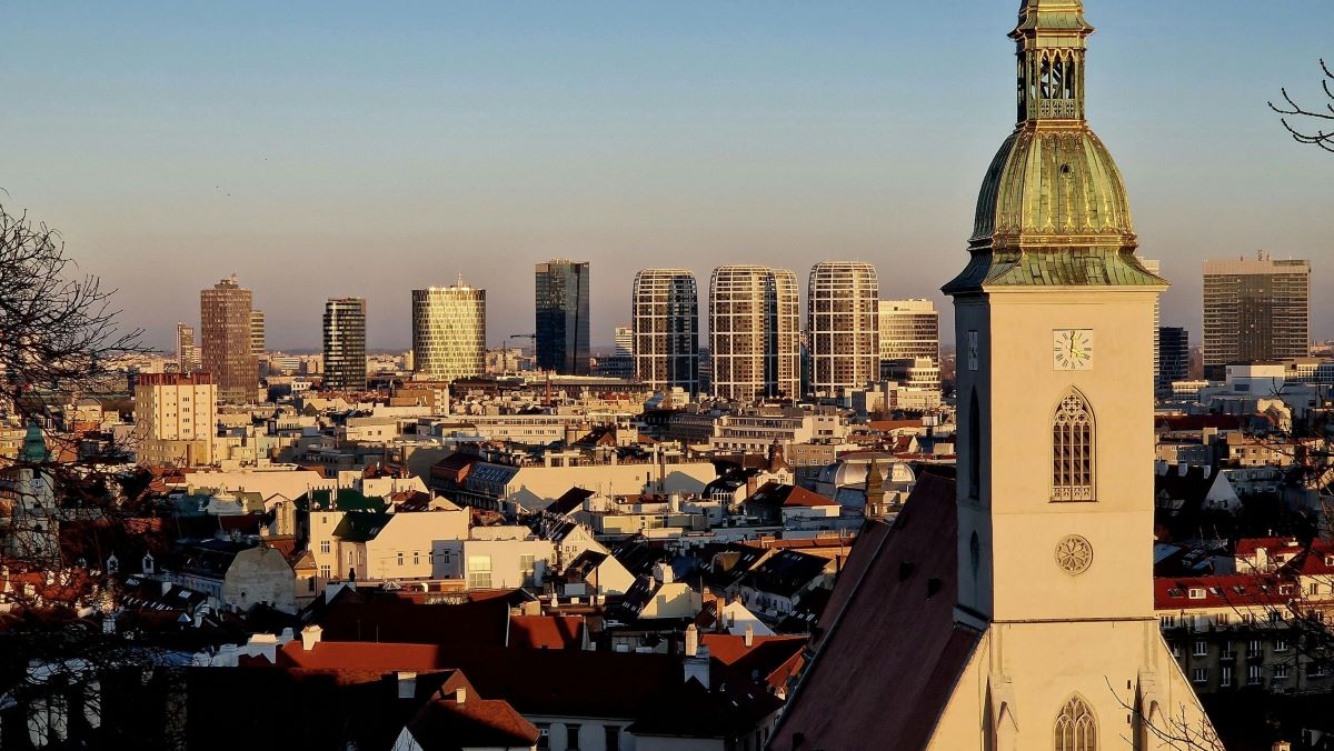 Pohľad z výšky na kostolnú vežu a mrakodrapy v Bratislave.