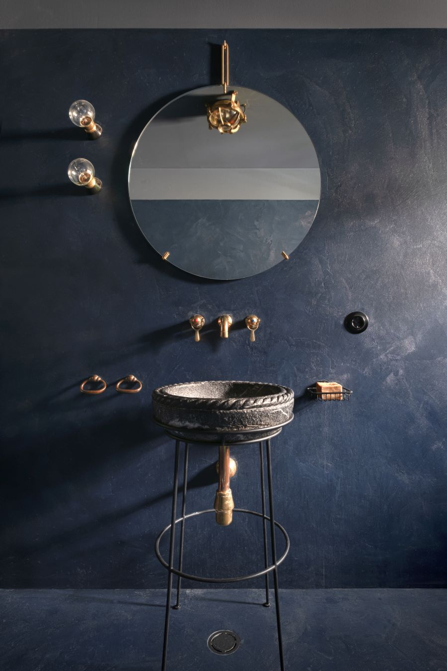 Staré kamenné umývadlo na kovovom stojane so zlatými doplnkami v tmavomodrej kúpeľni.