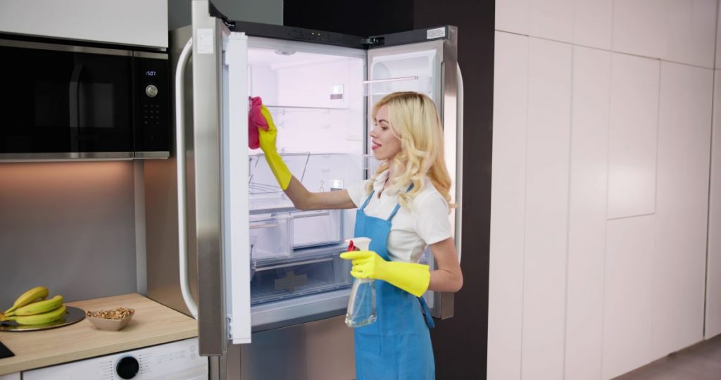 Žena v zástere čistí chladničku.