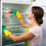 Žena v zástere čistí poličky v chladničke.