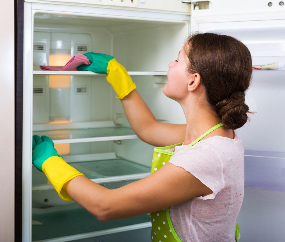 Žena v zástere čistí poličky v chladničke.