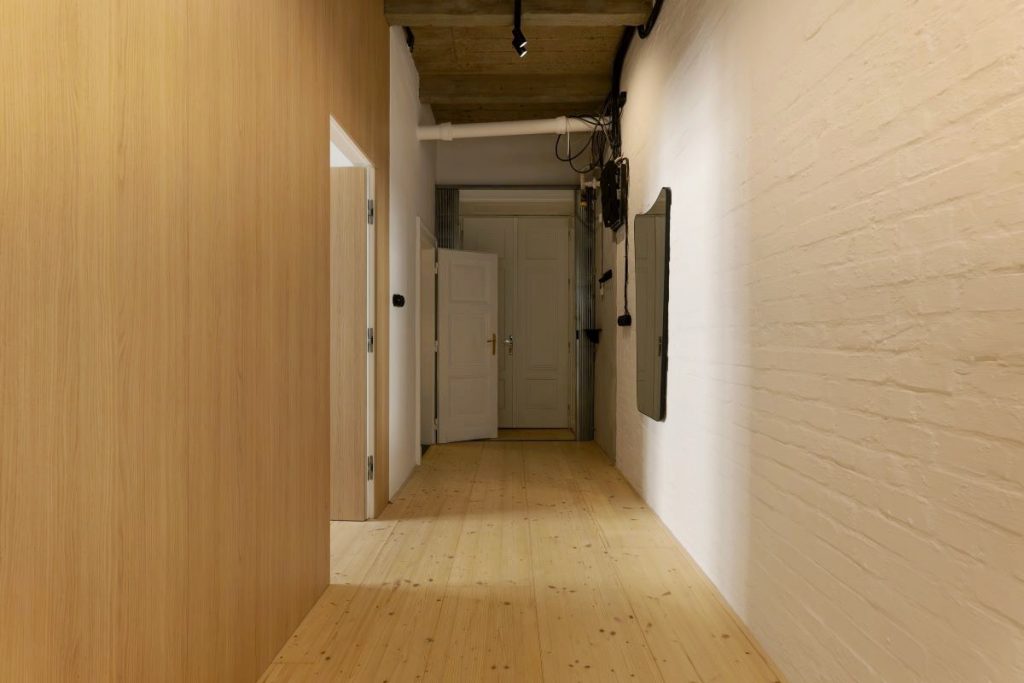 Vstupná chodba v byte s drevenou podlahou a nabielo natretou tehlovou stenou.