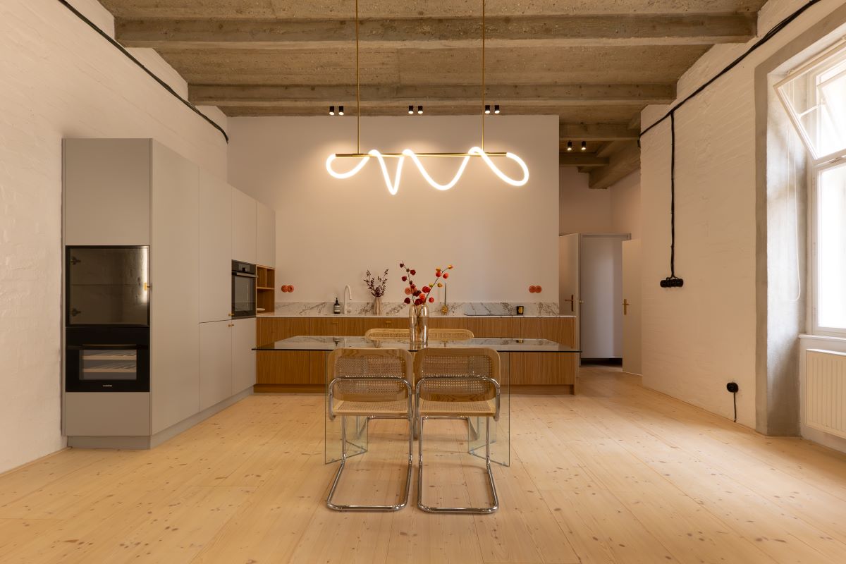 Moderná minimalistická kuchyňa so zabudovanými spotrebičmi a skleneným jedálenským stolom.
