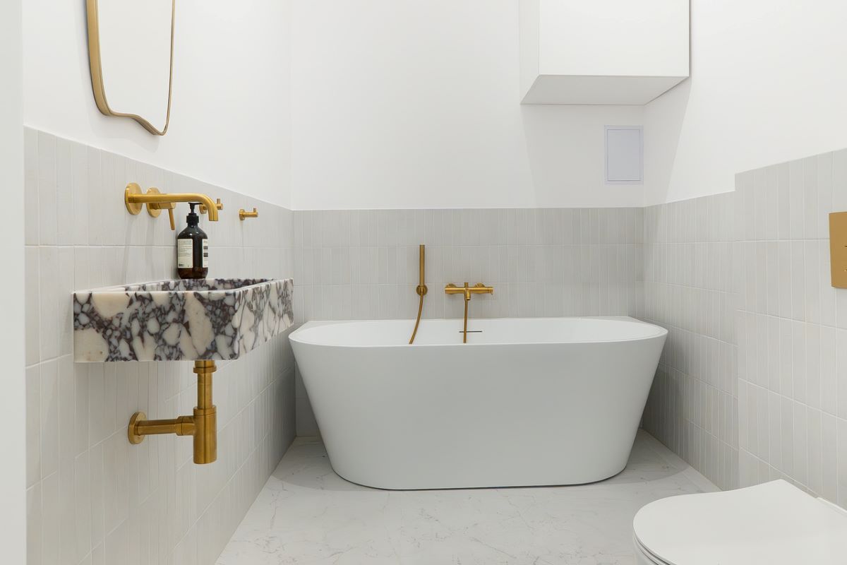 Kúpeľňa do samostatne stojacou vaňou, umývadlom z mramoru Calacatta Viola a zlatými doplnkami.