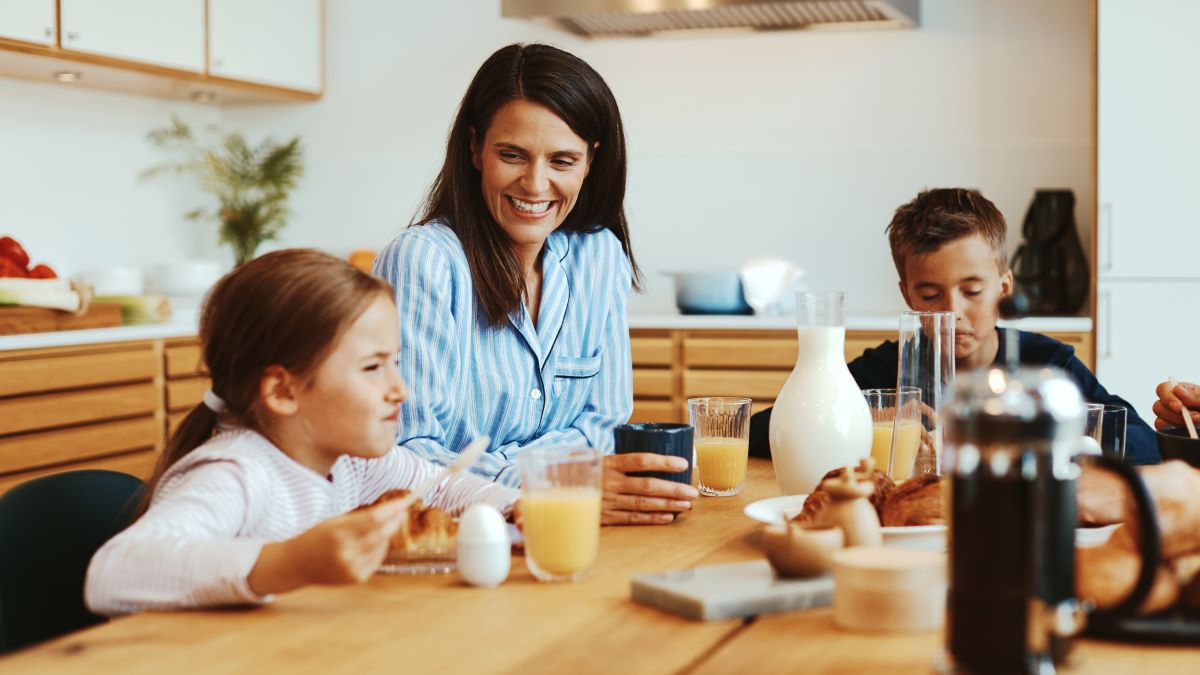 Matka s deťmi pri raňajkách za dreveným stolom.