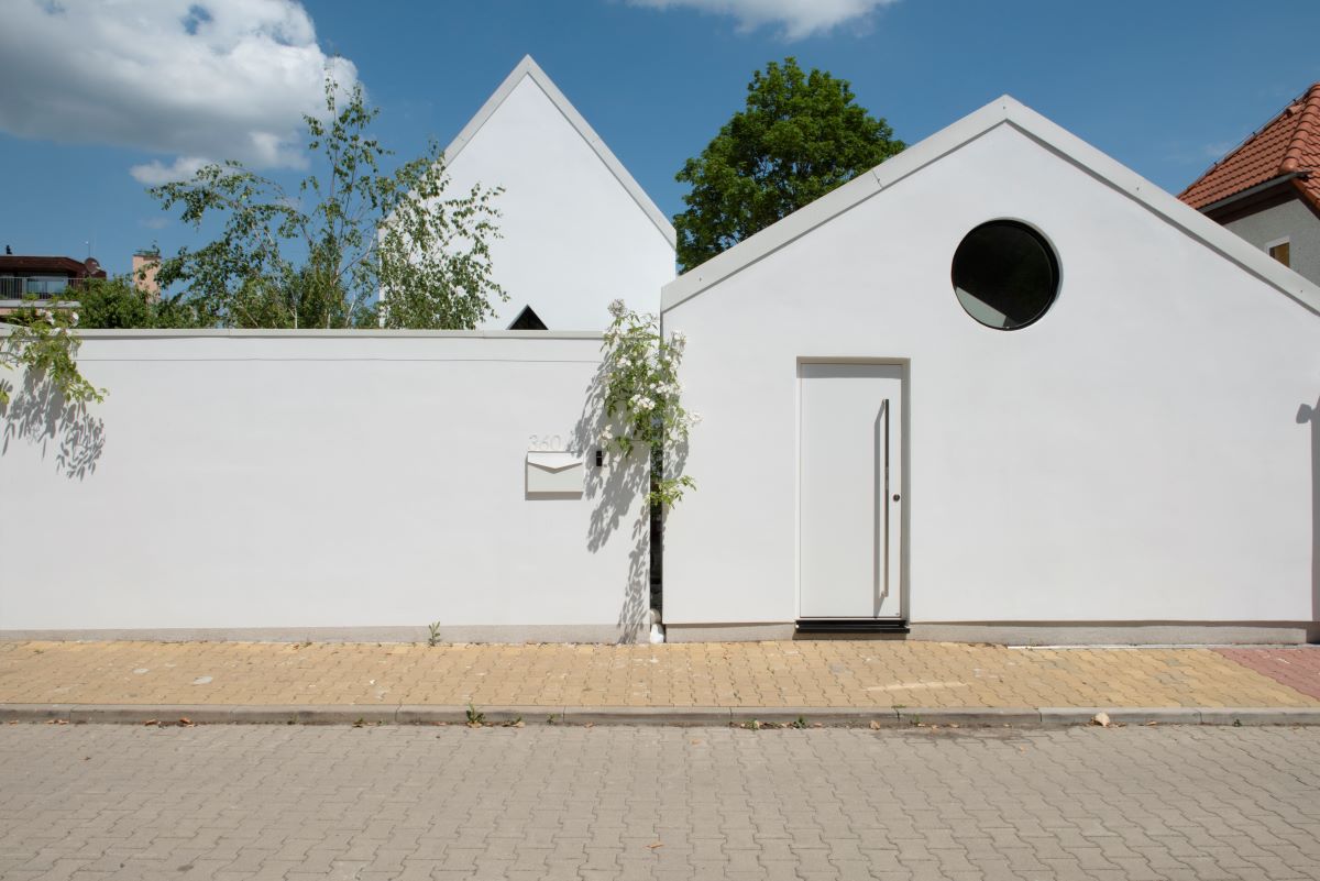 Moderná biela budova so sedlovou strechou a bielym murovaným plotom.