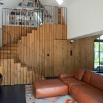 Pohodlná nadčasová obývačka s hnedou koženou sedačkou a dreveným schodiskom s kovovým zábradlím.