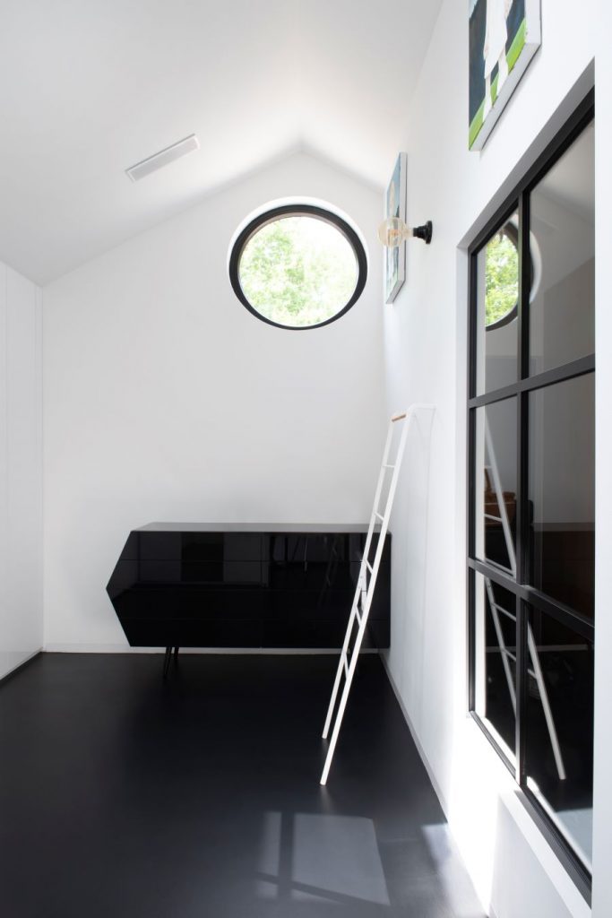 Priestranný čierno-biely šatník s rebríkom a okrúhlym oknom.