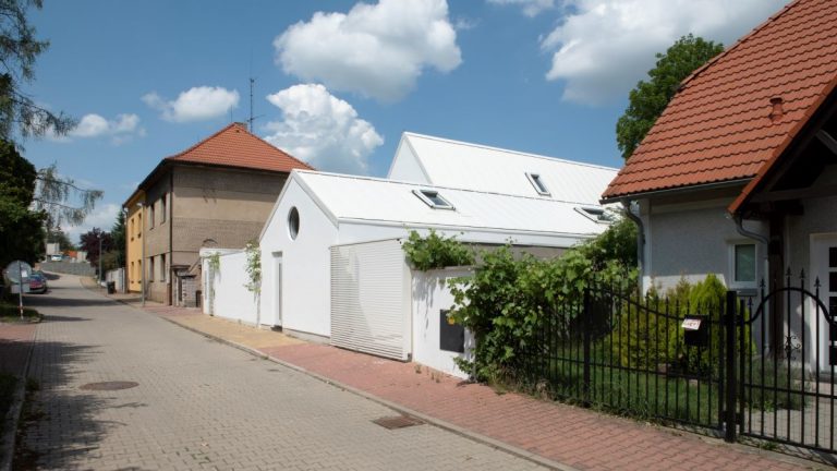Moderná biela budova vo vidieckej zástavbe so sedlovou strechou.