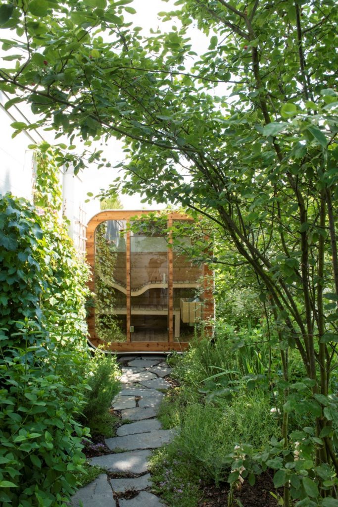 Moderná drevená sauna medzi zeleňou a stromami.