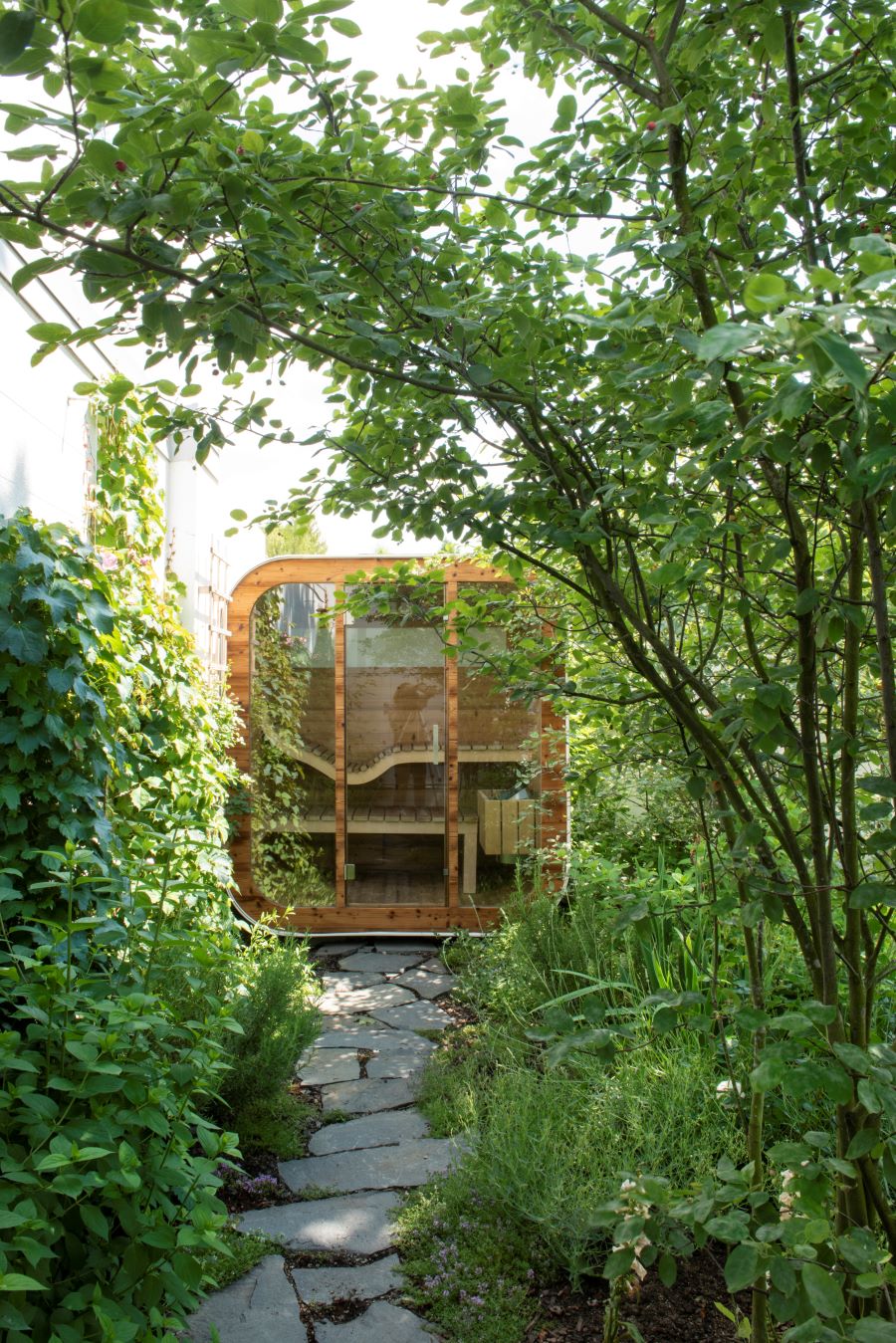 Moderná drevená sauna medzi zeleňou a stromami.