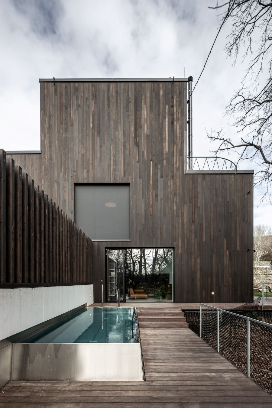 Exteriér rodinného domu s drevenou fasádou a bazénom na terase.