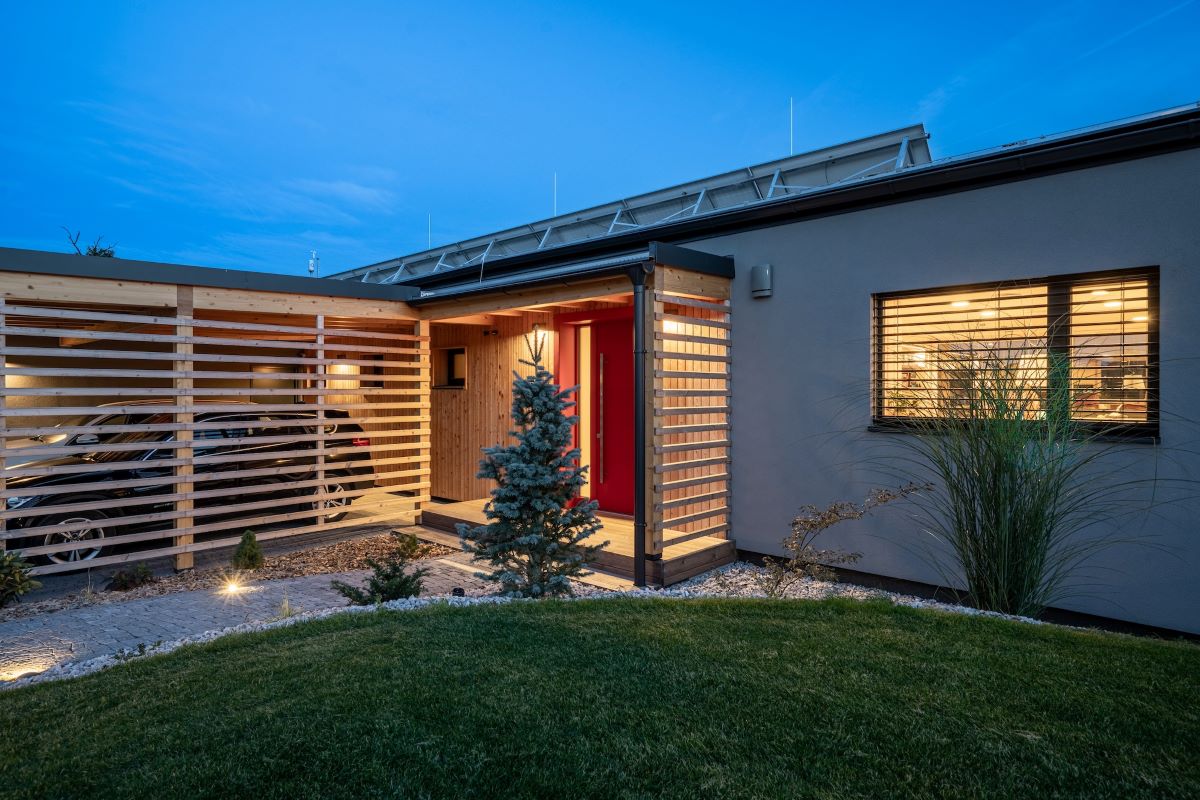 Vstup do moderného dreveného domu s osvetlenou terasou a garážou.