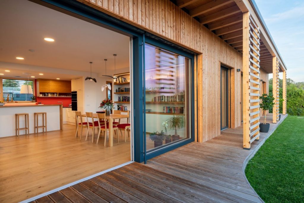 Krytá drevená terasa domu so vstupom do otvorenej kuchyne s jedálňou.