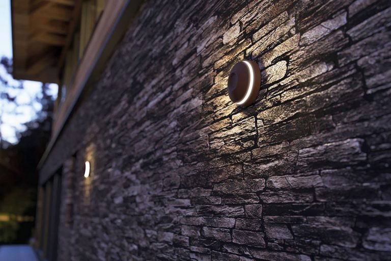 Moderné nástenné svietidlo na kamennej stene, osvetľujúce exteriér domu.