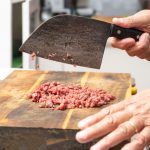Muž seká mäso veľkým kuchynským nožom na mäso.