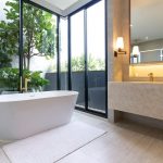 Moderná kúpeľňa s presklenými stenami s výhľadom na balkón, samostatnou vaňou a luxusným zariadením.
