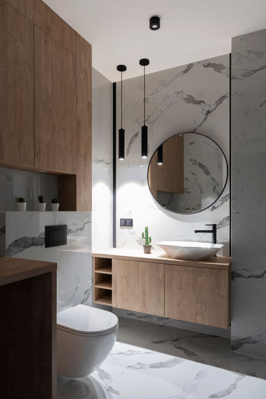 Moderná kúpeľňa s mramorovým obkladom a dreveným nábytkom, okrúhlym zrkadlom a modernými svietidlami.
