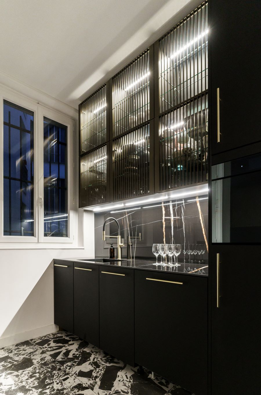 Moderná čierna kuchynská linka so zlatými detailmi a presklenými skrinkami.