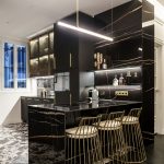 Moderná čierna kuchynská linka so zlatými detailmi a pultom s barovými stoličkami.