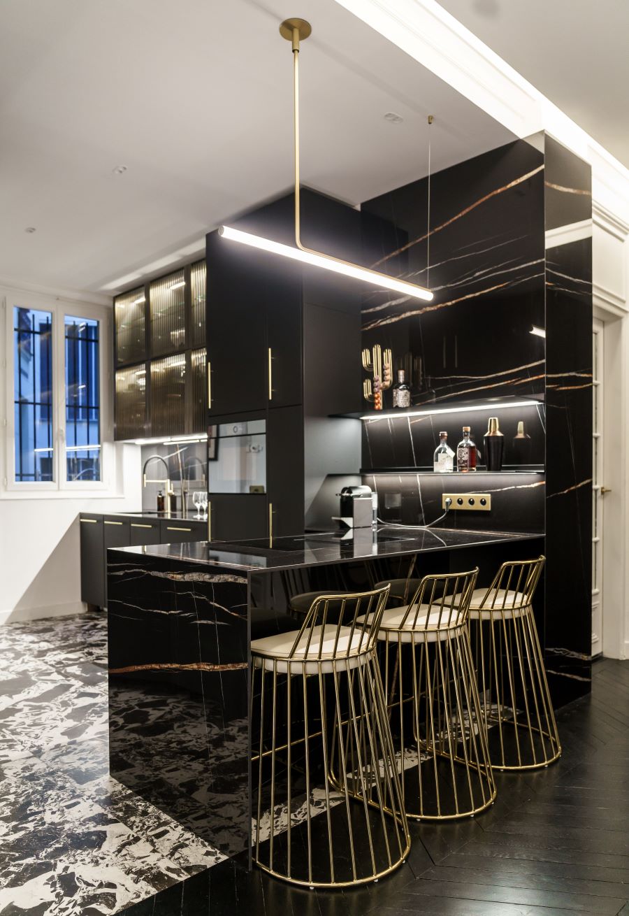Moderná čierna kuchynská linka so zlatými detailmi a pultom s barovými stoličkami.
