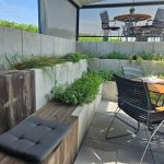 Členitý terén využitý na vytvorenie súkromia pri vonkajšom posedení na terase vinárstva v kombinácii pohľadového betónu, imitácii dreva a čiernym kovom vonkajšieho nábytku.