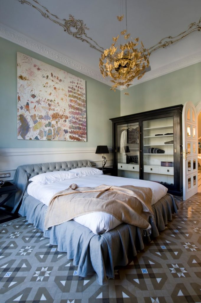Luxusná spálňa s elegantným lustrom a obrazom nad posteľou.