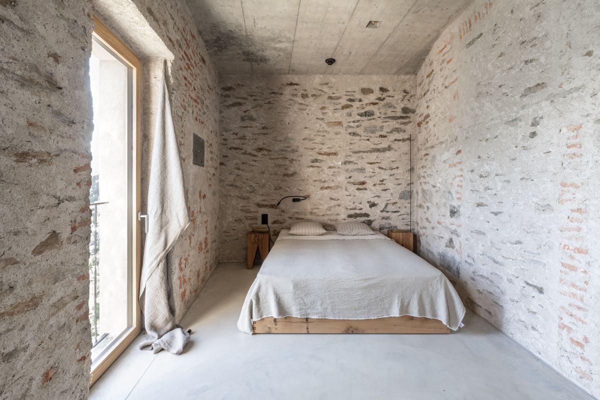 Spálňa so starými kamennými múrmi, drevenou posteľou a veľkým oknom s výhľadom na španielsky vidiek.