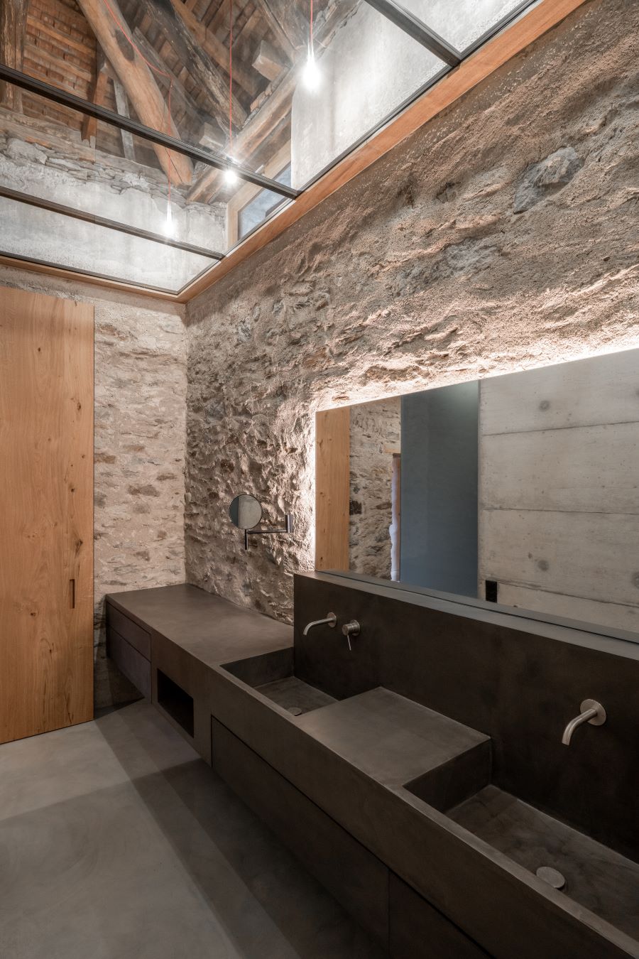 Moderná kúpeľňa s kamennými a betónovými stenami, minimalistickým umývadlom a preskleným stropom.