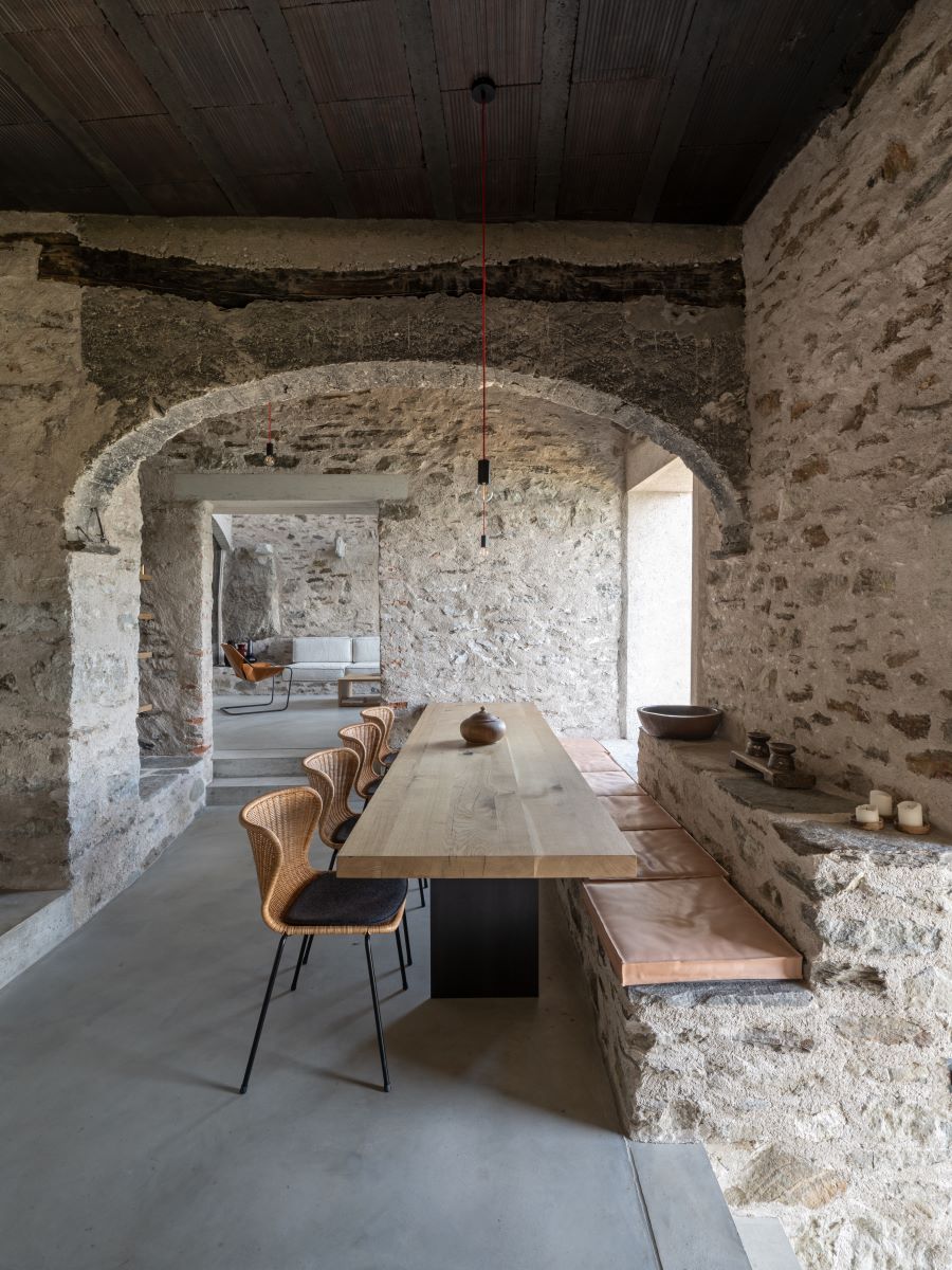 Rustikálna jedáleň s kamennými múrmi a dreveným stolom, presvetlená prírodným svetlom.
