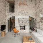 Obývačka v starom kamennom dome s vysokým stropom, kamennými múrmi, kozubom a moderným nábytkom.