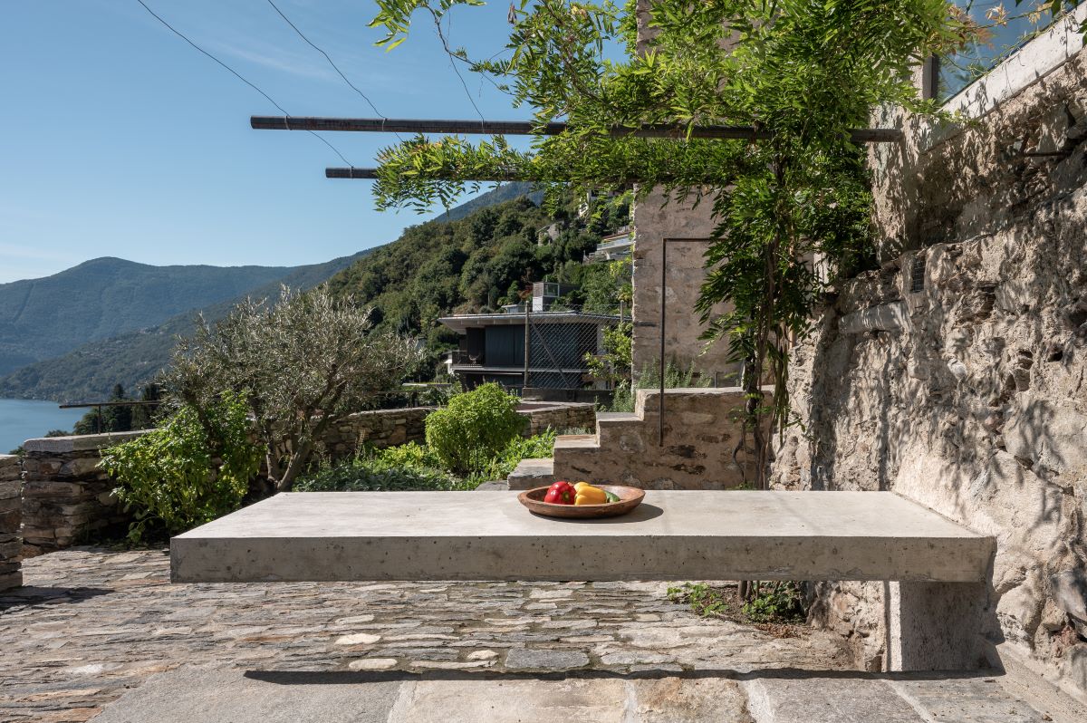 Vonkajší kamenný jedálenský stôl na kamennej terase s výhľadom na kopce a jazero.