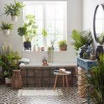 Svetlá kúpeľňa plná zelených rastlín s vaňou, dreveným nábytkom a dekoračnými prvkami.
