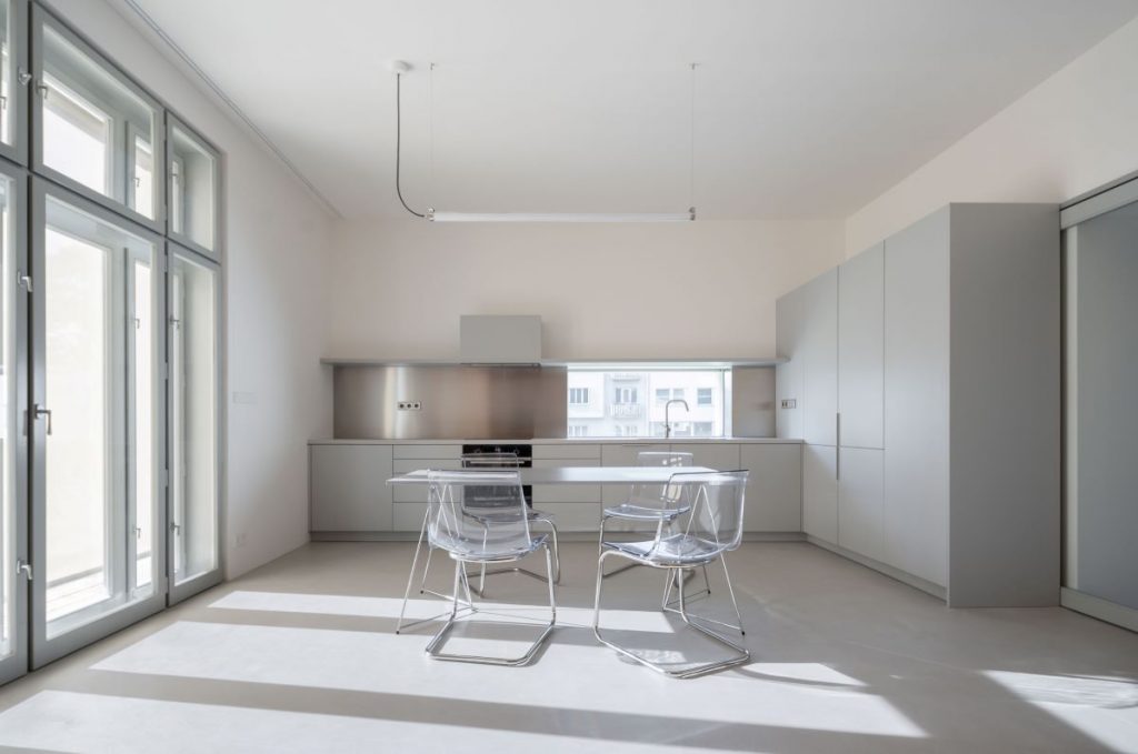 Minimalisticky zariadená kuchyňa v svetlosivej farbe s linku, jedálenským stolom a priehľadnými stoličkami.