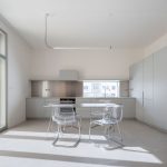 Minimalisticky zariadená kuchyňa v svetlosivej farbe s linku, jedálenským stolom a priehľadnými stoličkami.