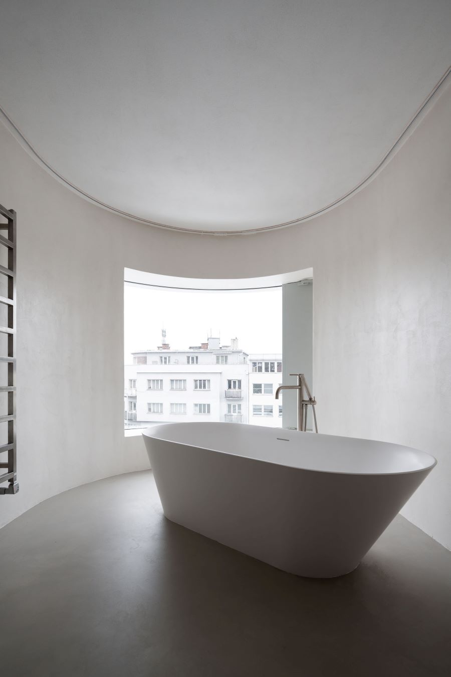 Minimalistická kúpeľňa v historickej vile na pražských Vinohradoch s modernou vaňou a oblým oknom.