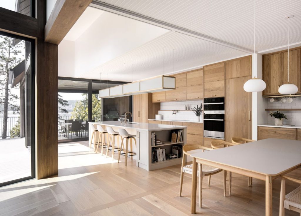 Moderná kuchyňa s veľkými oknami a linkou, ostrovom i zariadením v kombinácii dreva a bielej farby.
