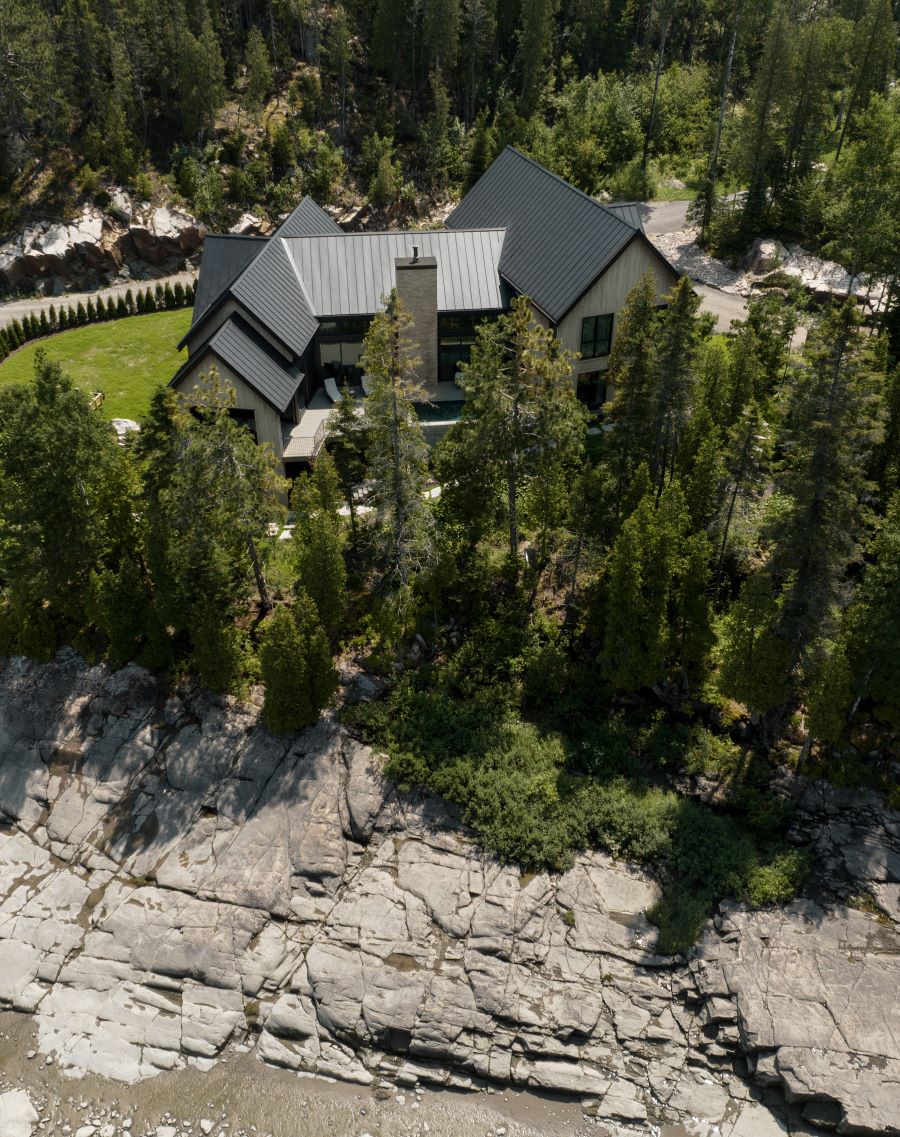 Pohľad z dronu na rodinný dom, pás stromov a skalnaté pobrežie fjordu.