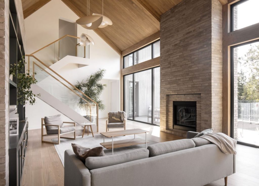 Priestranná obývacia izba s vysokým dreveným stropom, veľkými oknami a moderným kozubom pri nadčasovom sedení.