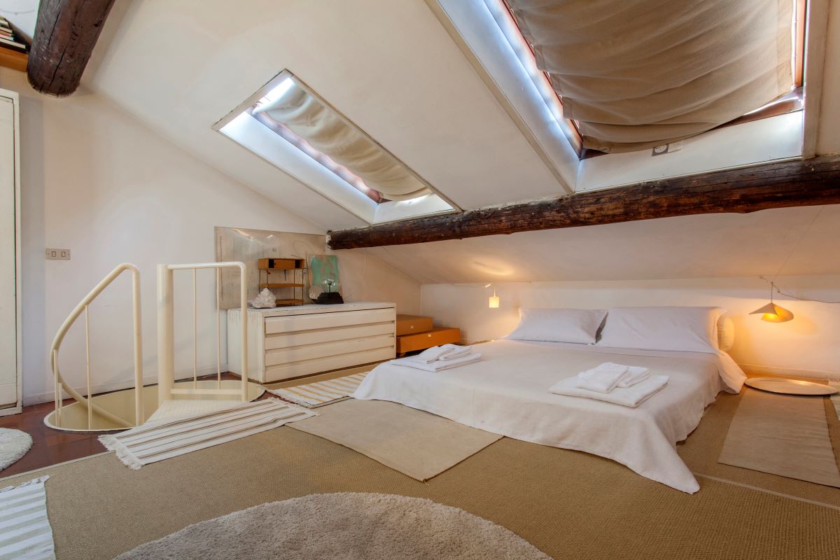 Nízka dvojlôžková posteľ z matracov a svetlá komoda v podkrovnej miestnosti.