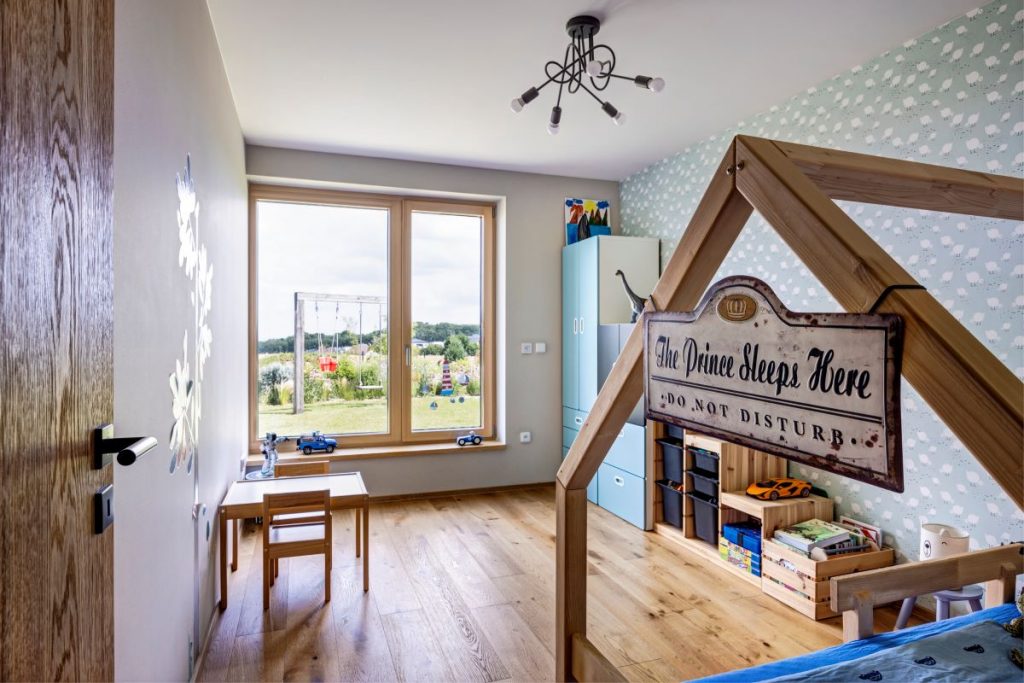 Moderne zariadená detská izba s bielymi stenami, drevenou podlahou, modrou tapetou a dreveno-modrým nábytkom.