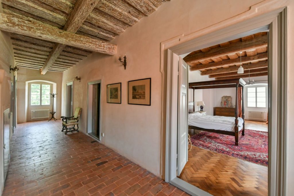 Chodba na poschodí s drevenými trámami, dlažbou na podlahe a vstupom do spálne v rekonštruovanej fare v Chudeniciach.