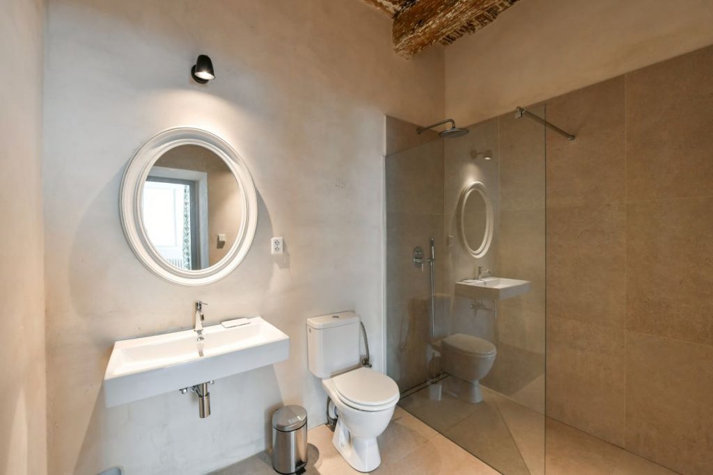 Moderná kúpeľňa s kruhovým zrkadlom a sprchovým kútom v zrekonštruovanej fare v Chudeniciach.